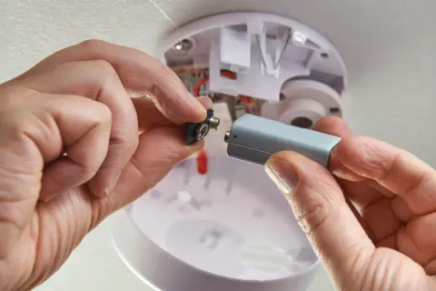 Hände wechseln Batterie eines Rauchmelders. Wichtig für die Versicherung und Sicherheit.