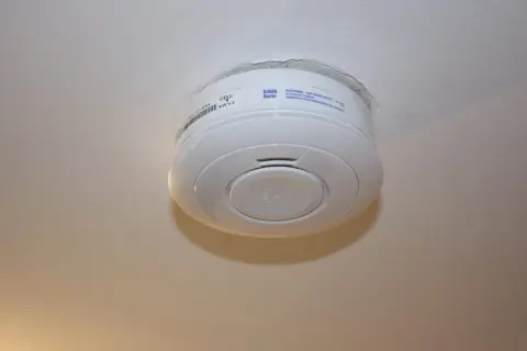 Ein weißer Rauchmelder hängt an der Decke. Er scheint von alleine auszugehen, da kein Alarm zu hören ist.