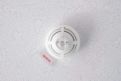 Rauchmelder an einer perforierten Decke. Sie reagieren auf Rauchpartikel in der Luft, um Brände frühzeitig zu erkennen.