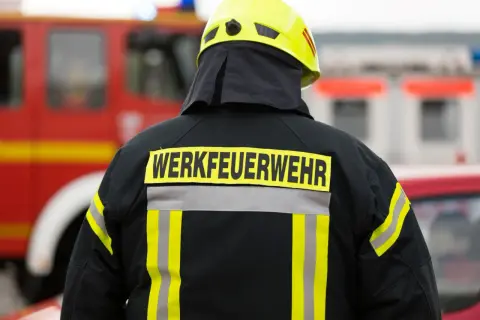 Rückansicht eines Feuerwehrmanns mit gelbem Helm und Jacke, auf der "WERKFEUERWEHR" steht. Dies zeigt, was eine Werkfeuerwehr ist: eine spezialisierte Feuerwehr für Industriebetriebe.