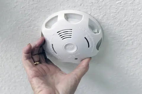 Ein weißer Rauchmelder wird von einer Hand gehalten. Er geht ohne Grund an und piept laut.