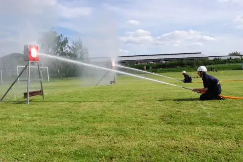 Feuerwehrleute üben einen löschangriff nass aufbau. Sie zielen mit Wasserschläuchen auf Ziele auf einem Feld.