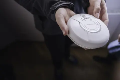 Eine Hand hält einen weißen Rauchwarnmelder. Dieses Gerät ist wichtig für die Sicherheit zu Hause.