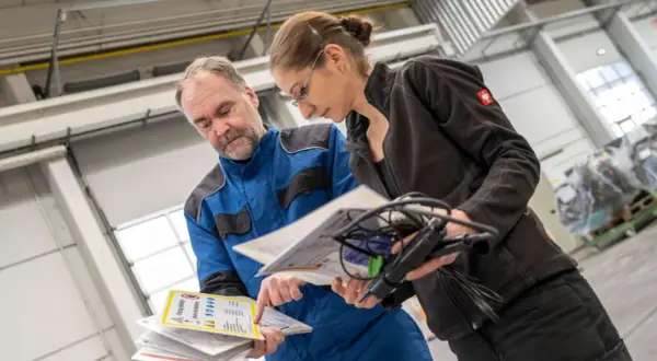 Mitarbeiter besprechen Dokumente zur Auffrischung Sicherheitsbeauftragter in einer Werkstatt.