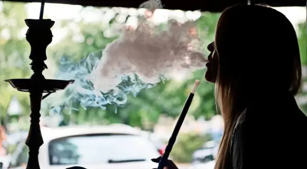 Silhouette einer Frau, die eine Shisha raucht. Dichter Rauch steigt auf und umhüllt ihr Gesicht. Ein **Rauchmelder** wäre hier fehl am Platz.