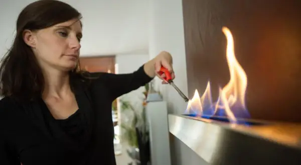 Frau zündet Ethanol-Kamin an. Die Flammen tanzen, ein Zeichen für Wärme und Gemütlichkeit, dank der Ethanol-Marke.