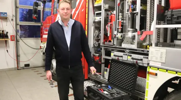 Mann vor Feuerwehrfahrzeug mit Werkzeugkoffer. Tolle Feuerwehr mitgliederwerbung ideen für Nachwuchs.