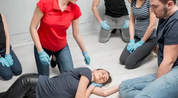 Erste-Hilfe-Kurs: Eine Frau wird in die stabile Seitenlage gebracht. Mehrere Personen mit blauen Handschuhen beobachten aufmerksam.