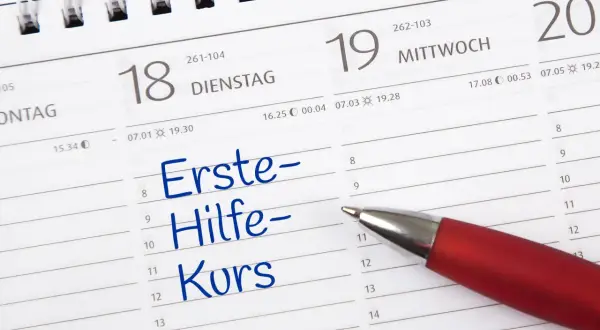 Ein roter Stift markiert "Erste-Hilfe-Kurs" in einem Kalender. Die Frage "wie lange gilt ein erste hilfe kurs" wird hier visuell thematisiert.