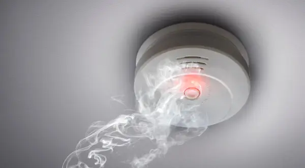 Rauchmelder mit rotem Licht und Rauch, der darauf hindeutet, wie viele Rauchmelder im Haus wichtig sind.