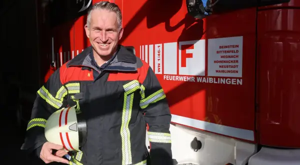Ein lächelnder hauptamtlicher feuerwehrkommandant in Uniform hält seinen Helm vor einem roten Feuerwehrauto.