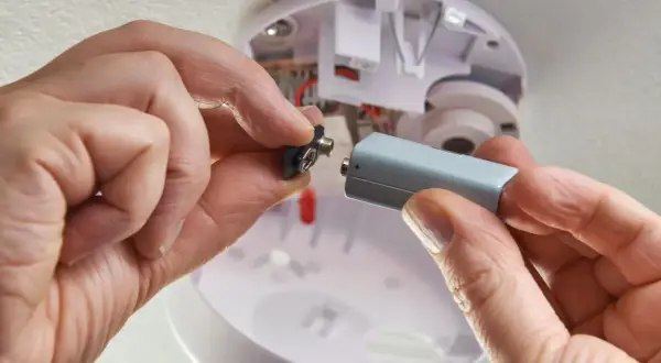 Hände wechseln die Batterie eines Rauchmelders, da die alte leer ist. Sicherheit geht vor!
