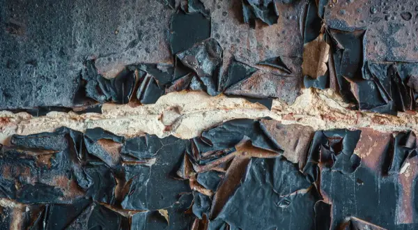 Abgeblätterte schwarze Farbe auf einer Ziegelwand, die auf eine Schadstoffmessung nach Brand hindeutet.