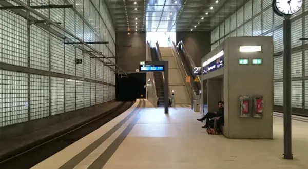 Moderne U-Bahn-Station mit Glaswänden, Rolltreppen und einer Uhr. Die Notbeleuchtung ist gemäß Vorschriften installiert.