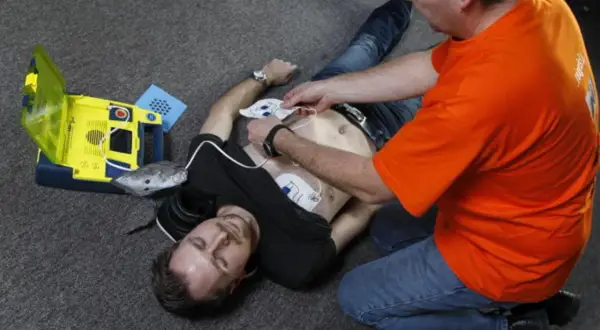 Mann legt Elektroden eines Defibrillators an, um Leben zu retten. Wann Defibrillator? Jetzt!