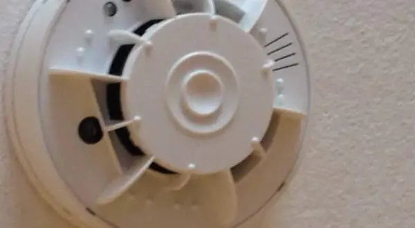 Ein weißer Rauchmelder mit integrierter Kamera, der an einer Decke montiert ist.