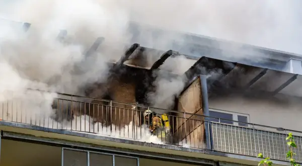 Feuerwehrleute kämpfen gegen einen Wohnungsbrand. Rauch quillt aus dem Gebäude. Ein Albtraum ohne Hausratversicherung.