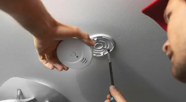 Mann schraubt Rauchmelder an Decke. Einfache Rauchmelder Wandmontage für mehr Sicherheit.