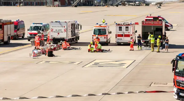 Einsatzkräfte von Feuerwehr und Katastrophenschutz üben am Flughafen. Mehrere Einsatzfahrzeuge, darunter ein Löschzug, sind vor Ort.