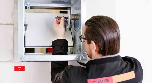 Techniker prüft die brandschutzklappe funktion. Er justiert eine Feder im Metallgehäuse, um die Sicherheit zu gewährleisten.