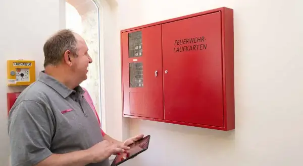 Mann prüft mit Tablet die Brandmeldeanlage. Regelmäßige Wartung sorgt für Sicherheit.