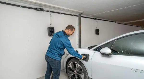 Mann lädt ein Elektroauto in der Garage. Die Installation ist für den Brandschutz ausgelegt.