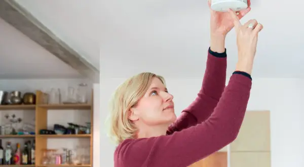 Frau montiert Rauchmelder nach DIN 14676 an der Decke.