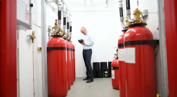 Mann prüft Brandschutz-System im Serverraum. Rote Gasflaschen sind für den Ernstfall bereit.