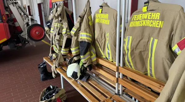 Schutzkleidung für die ehrenamtliche Feuerwehr hängt bereit. Stiefel und Helme liegen auf der Bank.