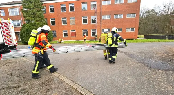 Feuerwehr-Messe: Einsatzkräfte transportieren eine Leiter vor einem Backsteingebäude. Eine Person steigt bereits eine Leiter zum Fenster empor.