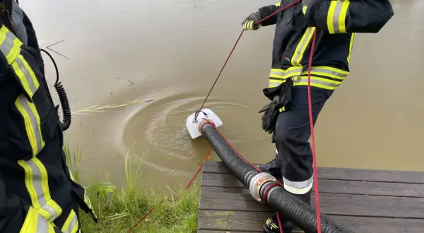 Feuerwehrleute führen eine wasserentnahme offenes gewässer fwdv 3 durch. Ein Tauchpumpen-Ansaugschlauch wird ins trübe Wasser gelassen.