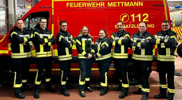 Feuerwehrleute in Mettmann, alle Altersgruppen, stehen stolz vor ihrem roten Einsatzfahrzeug.