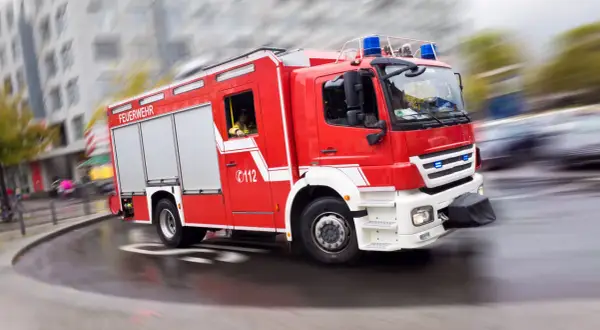 Rotes Feuerwehrauto mit Blaulicht rast durch die Stadt. Ein Feuerwehrmann am Steuer, bereit für den Einsatz. Rauchmelder sind wichtig, aber die Feuerwehr ist die ultimative Rettung.