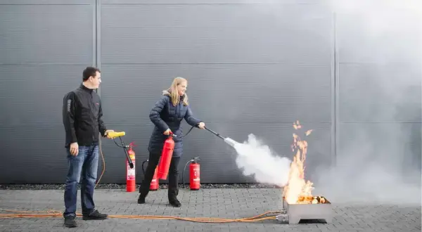 Frau übt mit Feuerlöscher bei Fortbildung Brandschutzhelfer. Mann beobachtet.