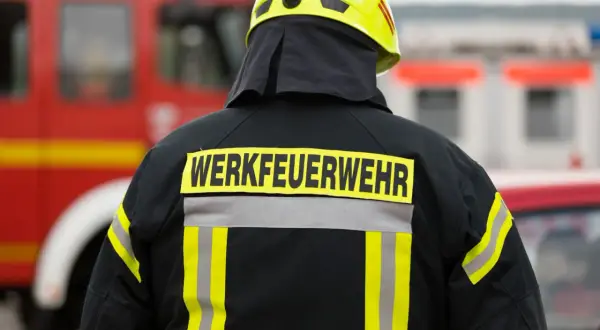 Rückansicht eines Feuerwehrmanns mit gelbem Helm und Jacke, auf der "WERKFEUERWEHR" steht. Dies zeigt, was eine Werkfeuerwehr ist: eine spezialisierte Feuerwehr für Industriebetriebe.