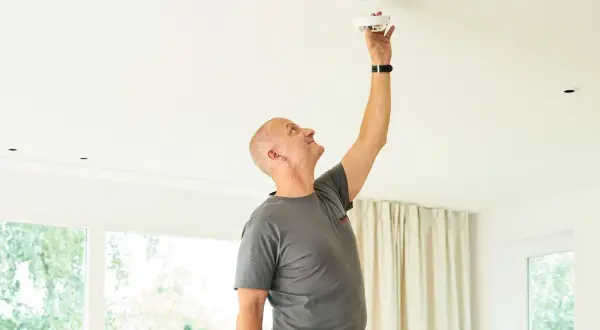 Mann montiert einen Rauchmelder an der Decke seiner Wohnung. Sicherheit geht vor!
