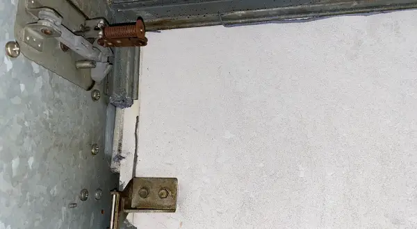 Detailaufnahme einer Brandschutzklappe mit sichtbaren mechanischen Teilen und einer weißen Platte. Möglicherweise Asbest-verdächtige Materialien.