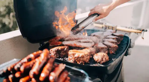 Leckeres Grillen auf dem Balkon: Würstchen und Steaks brutzeln auf dem Rost, Flammen lodern.