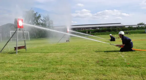 Feuerwehrleute üben einen löschangriff nass aufbau. Sie zielen mit Wasserschläuchen auf Ziele auf einem Feld.