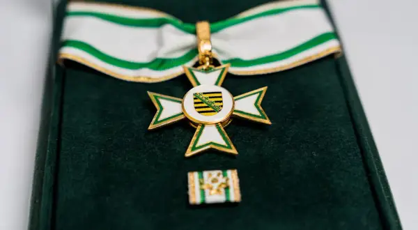 Ein goldenes Kreuz mit weißer und grüner Emaille, das ein Wappen mit schwarzen und gelben Streifen zeigt. Dieses Feuerwehr Ehrenzeichen liegt in einer grünen Samtschachtel.