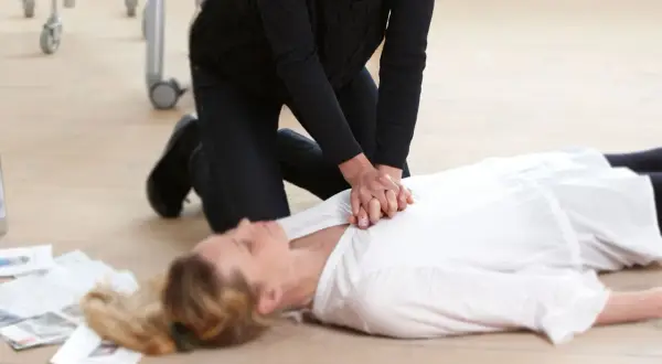 Erste Hilfe bei einem Schlaganfall: Eine Person kniet neben einer liegenden Frau und führt eine Herzmassage durch.