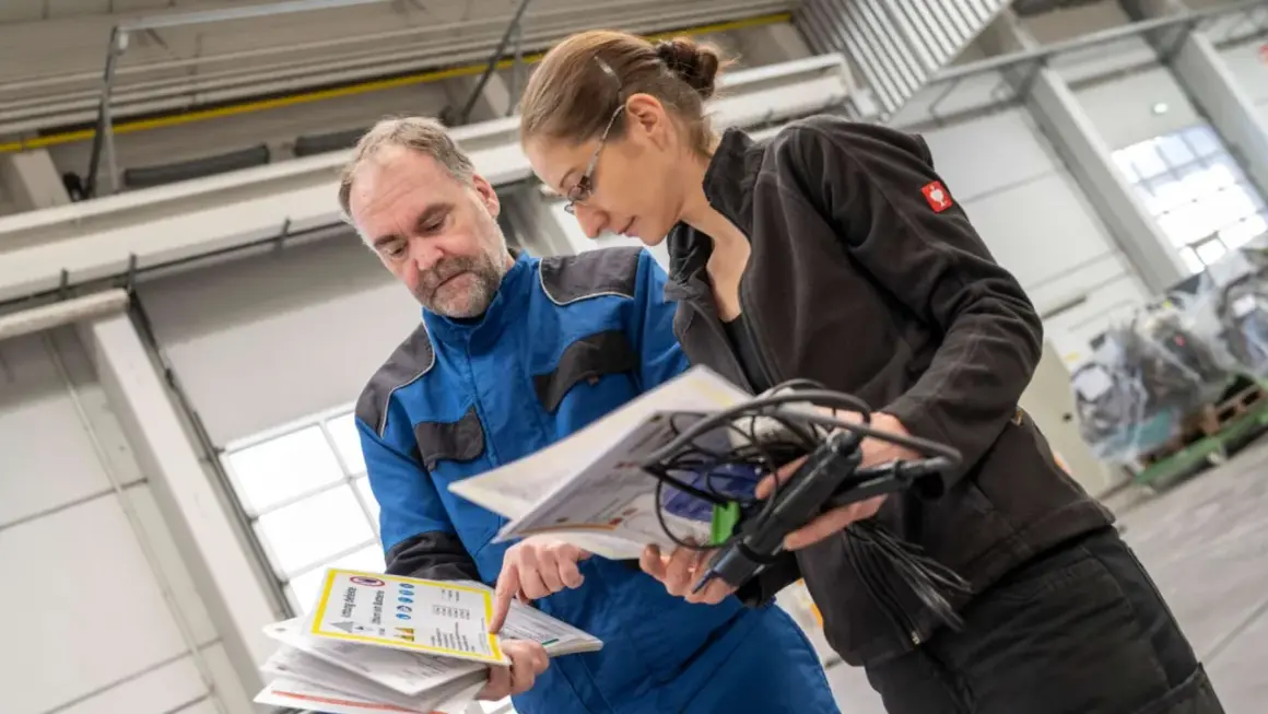 Mitarbeiter besprechen Dokumente zur Auffrischung Sicherheitsbeauftragter in einer Werkstatt.