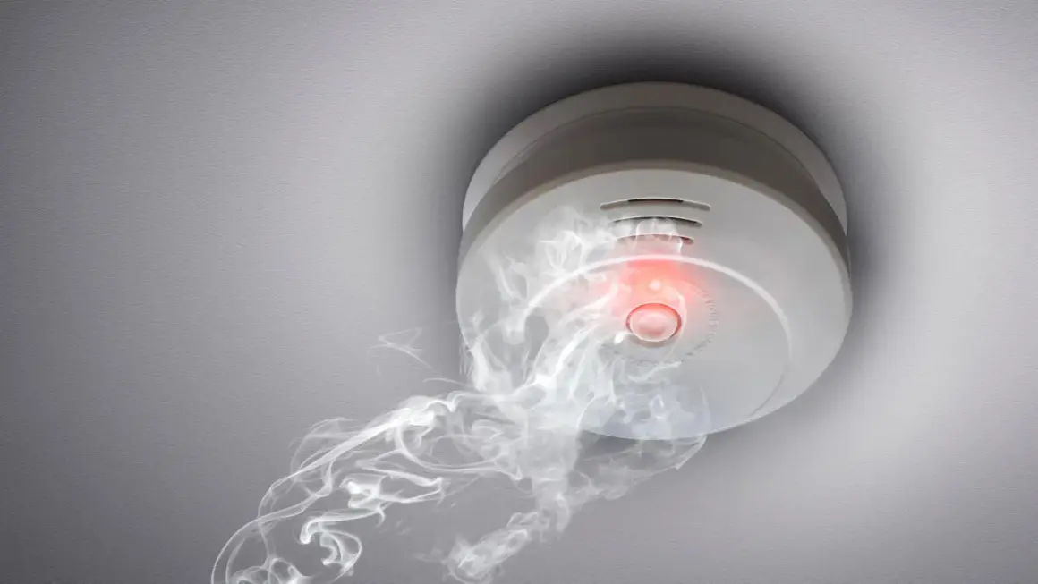 Rauchmelder mit rotem Licht und Rauch, der darauf hindeutet, wie viele Rauchmelder im Haus wichtig sind.