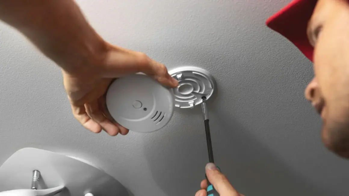 Mann schraubt Rauchmelder an Decke. Einfache Rauchmelder Wandmontage für mehr Sicherheit.