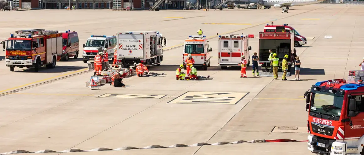 Einsatzkräfte von Feuerwehr und Katastrophenschutz üben am Flughafen. Mehrere Einsatzfahrzeuge, darunter ein Löschzug, sind vor Ort.