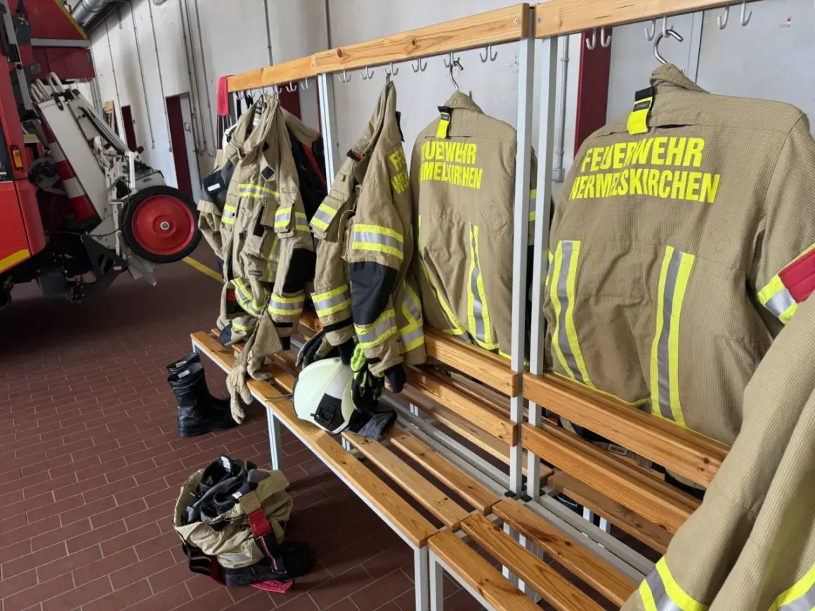 Schutzkleidung für die ehrenamtliche Feuerwehr hängt bereit. Stiefel und Helme liegen auf der Bank.