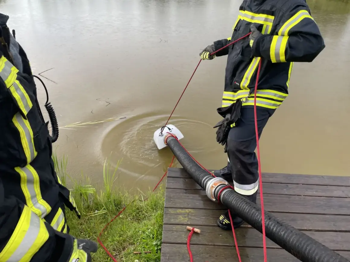 Feuerwehrleute führen eine wasserentnahme offenes gewässer fwdv 3 durch. Ein Tauchpumpen-Ansaugschlauch wird ins trübe Wasser gelassen.