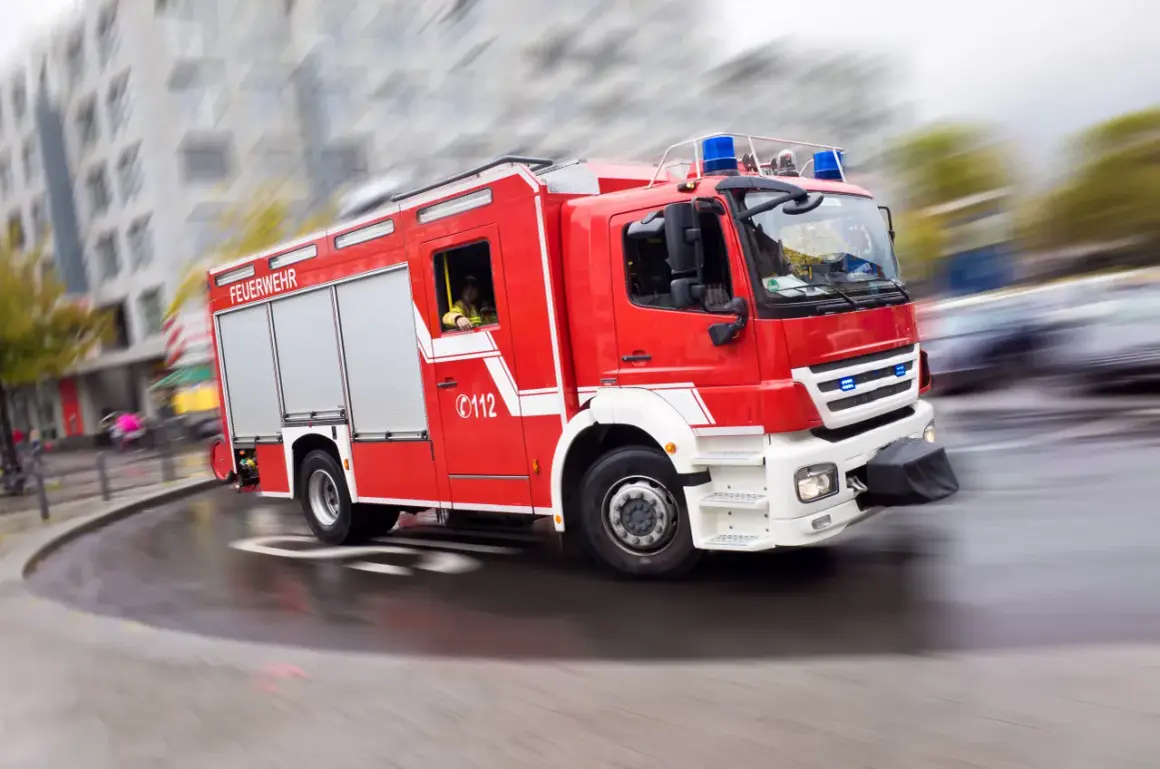 Rotes Feuerwehrauto mit Blaulicht rast durch die Stadt. Ein Feuerwehrmann am Steuer, bereit für den Einsatz. Rauchmelder sind wichtig, aber die Feuerwehr ist die ultimative Rettung.