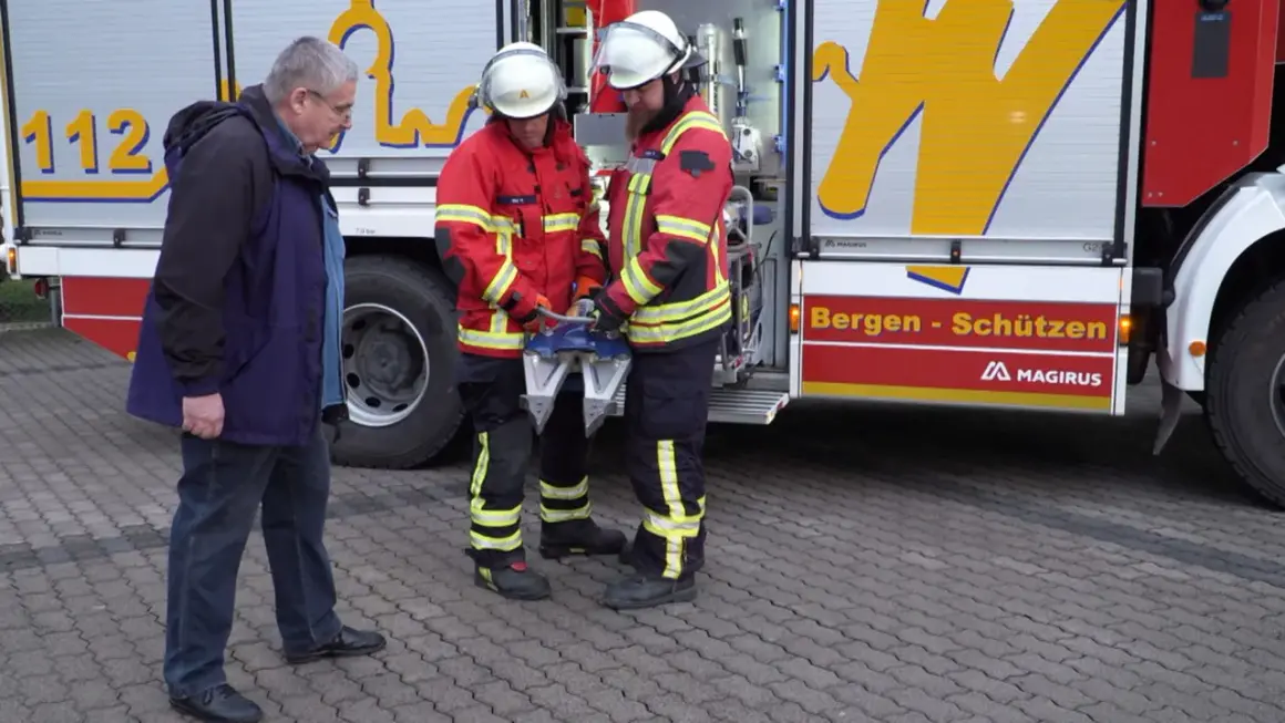 Zwei Feuerwehrmänner mit Rettungsgerät, ein Mann in Zivil. Frage: ab wann darf man bei der freiwilligen feuerwehr einsätze mitfahren?