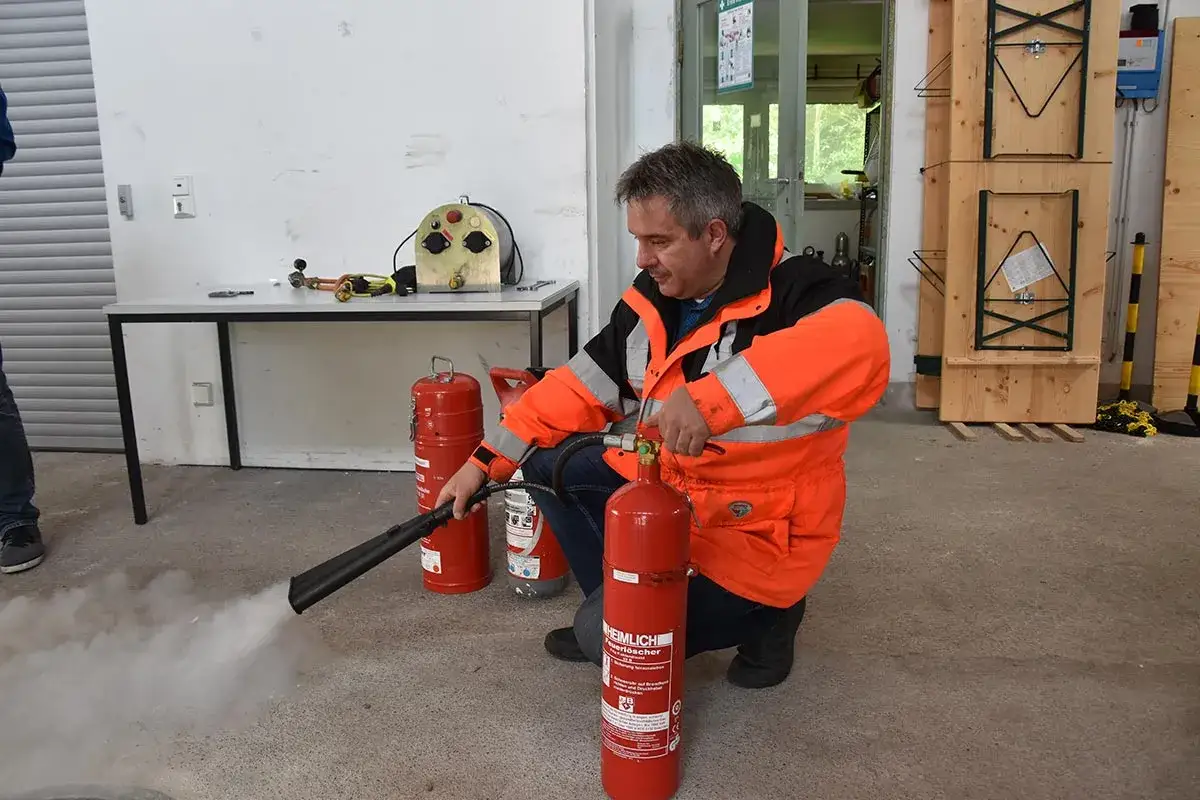 Mann in Warnweste übt mit Feuerlöscher. Auffrischung Sicherheitsbeauftragter im Einsatz.